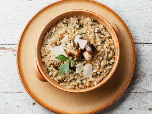 Un cremoso risotto ai funghi, un clásico plato italiano, servido en un cuenco de cerámica.