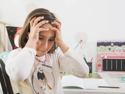 Dziewczynka z rękami na głowie, zmartwiona nauką. Jak rozładować stres u dziecka? Może przerwa na zabawę?