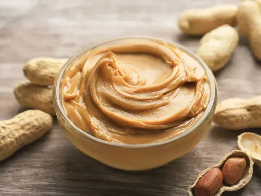 Cremige Erdnussbutter in einer Schüssel, umgeben von Erdnüssen. Ein Beweis dafür, dass erdnussbutter gesund sein kann, wenn sie in Maßen genossen wird.