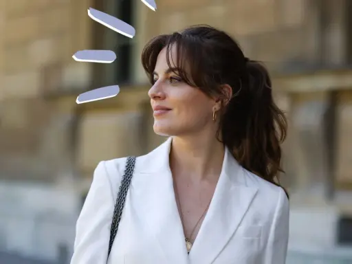 Frauen mit Curtain Bangs stylen ihre Haare lässig zu einem Pferdeschwanz. Der weiße Blazer unterstreicht den eleganten Look.