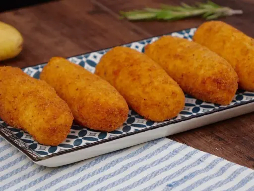 Cinque crocchette di patate dorate e croccanti su un piatto decorato, pronte per essere gustate.