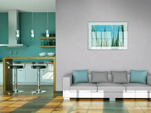 Modernes Wohnzimmer mit Vliestapete tapezieren. Ein weißes Sofa mit blauen und grauen Kissen steht vor einer Wand mit einem Bild von Gräsern. Daneben eine Küche mit Bar.