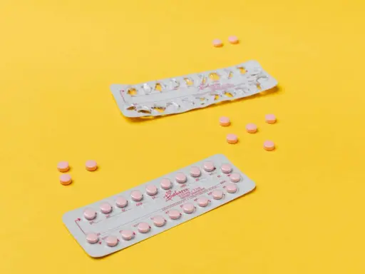 Dos blísteres de pastillas anticonceptivas y varias pastillas sueltas, rosas, sobre fondo amarillo. Ayudan a regular la regla.