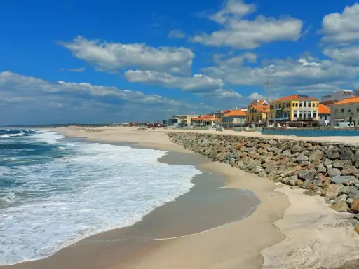 Sonne, Sand und Wellen an der Costa Verde, Portugal. Häuser mit roten Dächern säumen den Strand, geschützt von einer Steinmauer.