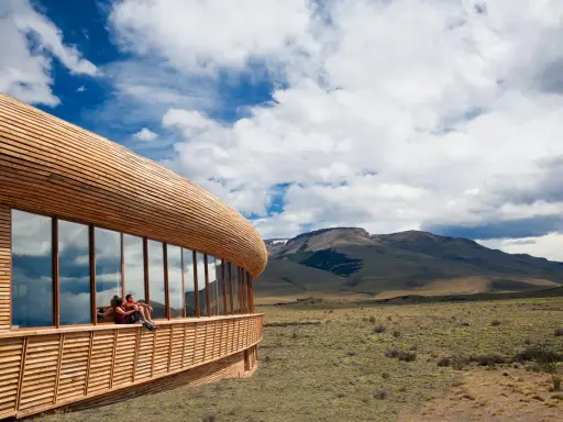 Coppia seduta su una terrazza di **edifici in legno famosi**, con vista su un paesaggio montano e cielo nuvoloso.