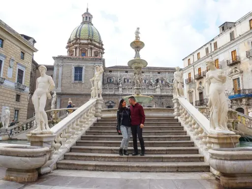 Coppia felice davanti alla Fontana Pretoria, un luogo imperdibile da vedere a Palermo, con le sue statue e la cupola in lontananza.
