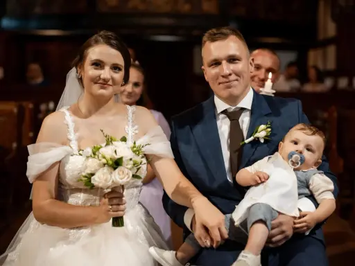 Para młoda z dzieckiem na rękach, podwójna uroczystość: ślub i chrzest w jednym.