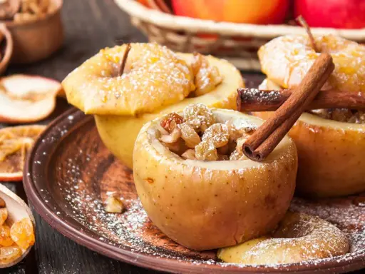 Manzanas asadas rellenas de pasas y canela, espolvoreadas con azúcar glas. Un postre casero y reconfortante.
