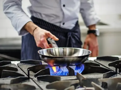 Chef calienta sartén de acero inoxidable para cocinar sobre llama azul de gas.