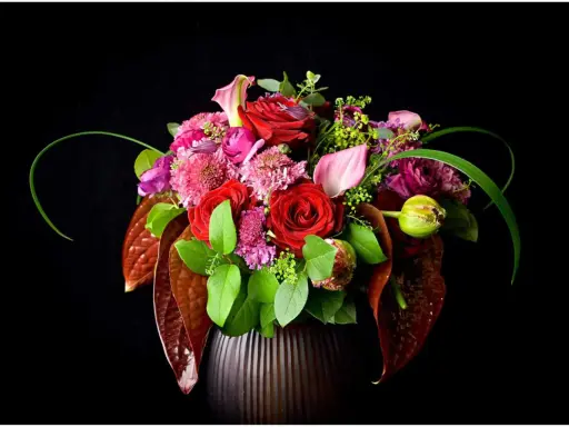 Un bouquet de roses rouges, callas roses et fleurs violettes dans un vase sombre. La signification des fleurs est souvent liée à l'amour et à la passion.