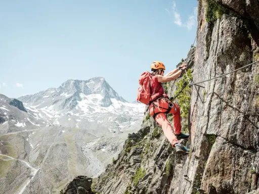 Wspinaczka po skalnej ścianie na via ferrata w Niemczech. Widok na ośnieżone góry w tle.