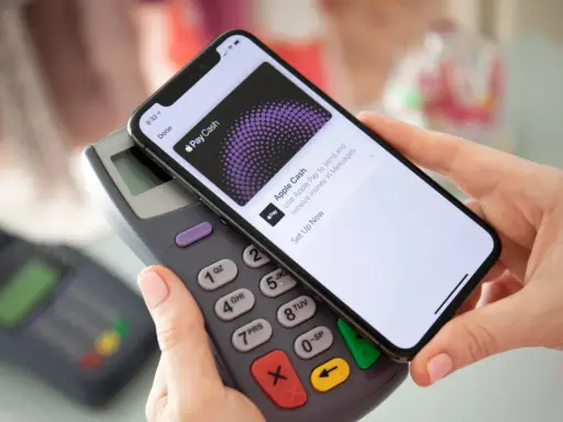 Dłoń zbliża telefon do terminala płatniczego, pokazując ekran Apple Pay. Tak łatwo można płacić telefonem.
