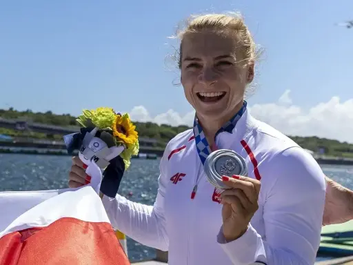 Uśmiechnięta sportsmenka z medalem i bukietem kwiatów, symbol sukcesu najlepszych polskich kajakarzy.