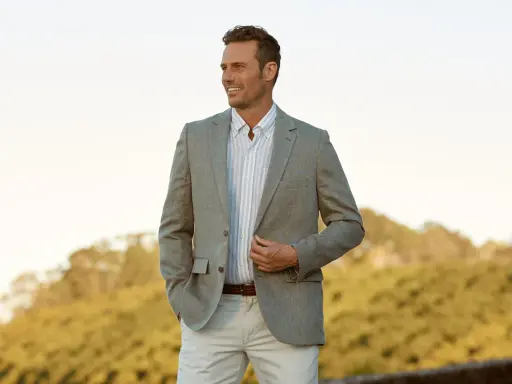 A man in a light grey blazer, striped shirt, and beige pants. This is a stylish option for what to wear to an engagement party.