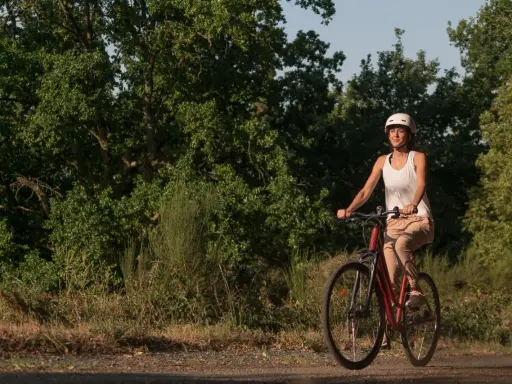 Kobieta w kasku i białej koszulce jedzie na rowerze po leśnej ścieżce. Odkrywa urokliwe trasy rowerowe Wrocławia.