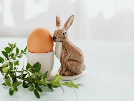 Wielkanocne jajka w kieliszku, obok ceramiczny zajączek i gałązka bukszpanu.