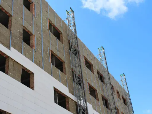 Fachada de edificio en construcción, con aislamiento térmico y andamios. Un plan rehabilita la estructura para mejorar su eficiencia energética.