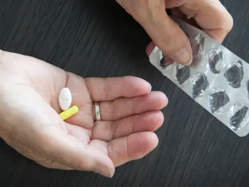 Dłoń trzyma białą i żółtą tabletkę, obok pusty blister. Może to być cytrynian magnezu.