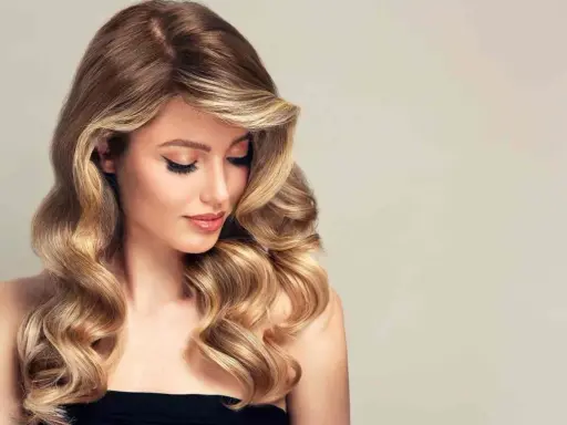 Kobieta z falowanymi, brązowo-blond włosami, delikatnym makijażem i spojrzeniem skierowanym w dół.
