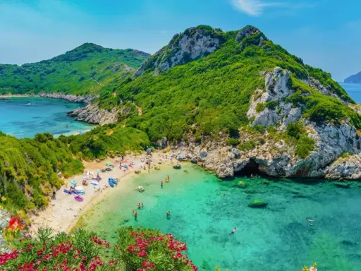 Malownicza zatoka z piaszczystą plażą, turkusową wodą, zielonymi wzgórzami i kwitnącymi kwiatami.