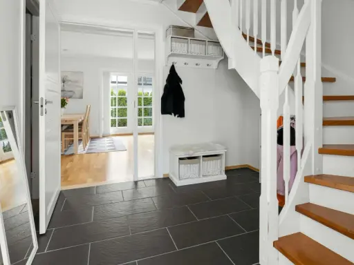 Helle Diele mit dunklem Fliesenboden, Spiegel, Garderobe und einer weißen Treppe, die auf eine **steintreppe renovieren**-Idee hindeutet.