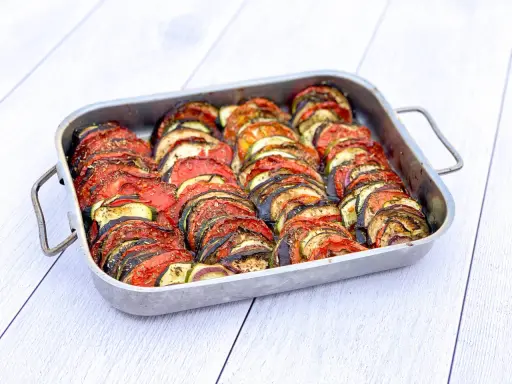 Un plat de tian de légumes, prêt à cuire, avec des rondelles de courgettes, aubergines et tomates joliment disposées. Parfait pour faire un tian de légumes la veille.