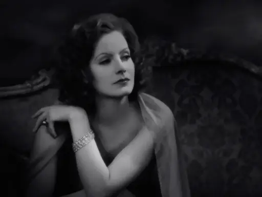 Elegancka Greta Garbo, z błyszczącą bransoletką, spogląda zamyślona z antycznej kanapy.