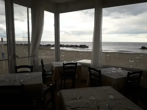 Tavoli apparecchiati in un ristorante con vista sulla spiaggia di Misano durante la bassa marea.
