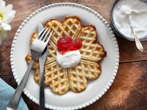 En vacker, hjärtformad våffla, perfekt för en fika. Dessa glutenfria våfflor serveras med vispad grädde och sylt.