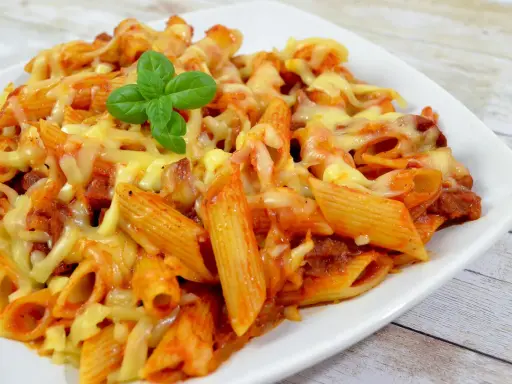 Penne z sosem pomidorowym i kawałkami pikantnego chorizo, zapieczone pod ciągnącym się serem, ozdobione listkiem bazylii.