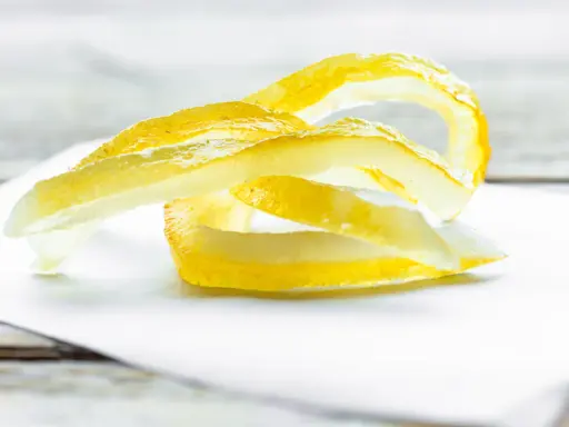 Gelbe Zitronenschalen-Streifen, die an das Selbermachen von Apfelpektin erinnern, liegen auf weißem Papier.