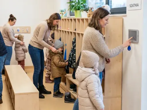 Rodzice odbierają dzieci z przedszkola. W szatni panuje ruch, dzieci ubierają się do wyjścia.