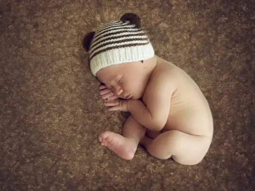 Śpiące dziecko w czapce z uszkami, zwinięte w kłębek. Wygląda, jakby na niczym mu nie zależało, pogrążone w błogim śnie.