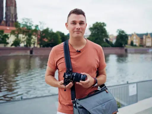 Mężczyzna z aparatem w rękach, na tle rzeki i zabytkowych budynków. Jakość 4k jaka to rozdzielczość, idealna do uchwycenia detali.
