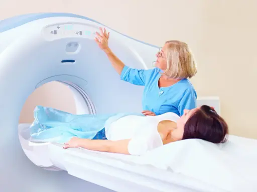 Pacjentka leży na stole do rezonansu magnetycznego. Technik obsługuje panel sterowania, przygotowując badanie rezonans magnetyczny kręgosłupa piersiowego.