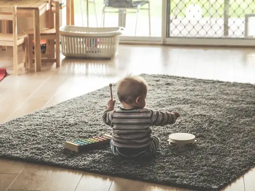 Liten bebis sitter på en matta och leker med en xylofon och en tamburin. En perfekt start på en checklista bebis för musikaliska äventyr.
