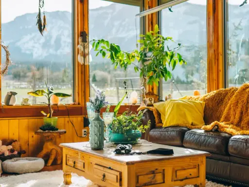 Un acogedor **salón estilo natural** con sofá de cuero, manta naranja, plantas y vistas a la montaña.