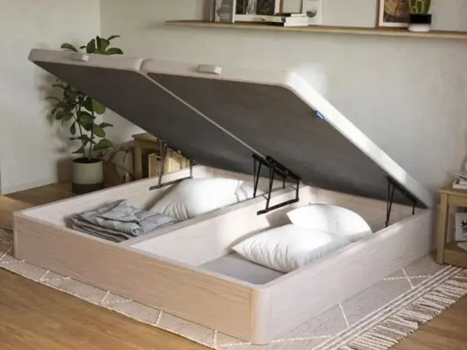 Un canapé de madera clara con la tapa abierta, revelando un gran espacio de almacenamiento para ropa de cama y almohadas.