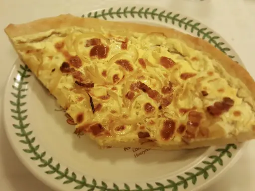 Part de quiche lorraine, une des spécialités lorraines, sur une assiette décorée de feuilles vertes.