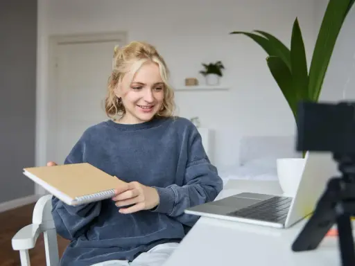 Junge Frau gibt online Nachhilfe, hält ein Notizbuch und lächelt in die Kamera.