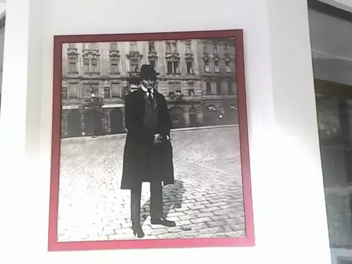 Ritratto di Franz Kafka, figura iconica che ci fa chiedere chi era Kafka, in piedi su un selciato con un edificio sullo sfondo.