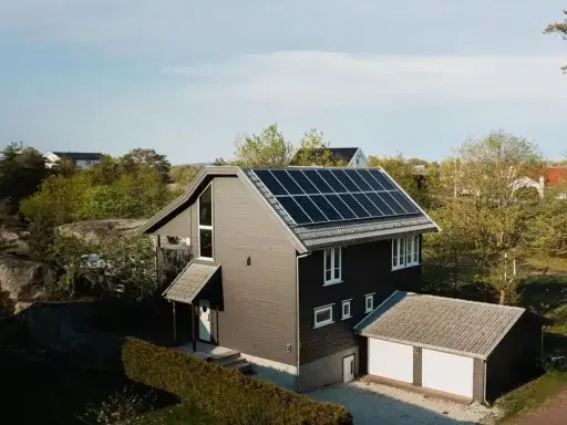 Ett modernt hus med mörk fasad och ett tak täckt av solceller. Bredvid huset finns ett garage med vita portar.