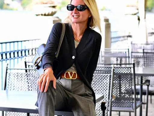 Donna con pantalone grigio elegante, abbinato a cardigan scuro e cintura con logo dorato. Un look chic per ogni occasione.