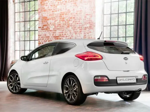 Biały Kia pro_ceed 1.6 CRDi z eleganckimi felgami stoi w stylowym wnętrzu z ceglaną ścianą i dużymi oknami.