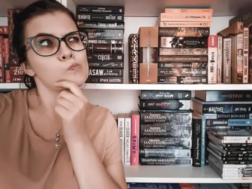 Dziewczyna z okularami zastanawia się nad wyborem książki. Na półkach obok kryminały, fantasy i erotyka subtelna.
