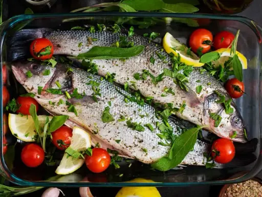 Dos lubinas enteras preparadas para ser horneadas, con tomates cherry, rodajas de limón y hierbas frescas.