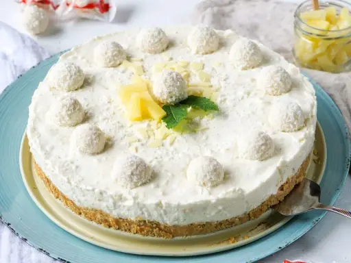 Eine köstliche Raffaello Torte ohne Backen, dekoriert mit Kokosbällchen, Ananas und Minze.
