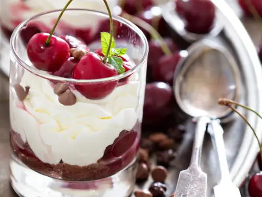 Delicioso postre con capas de crema batida, bizcocho de chocolate y cerezas frescas, coronado con más cerezas y trocitos de chocolate.