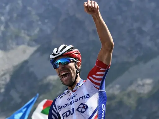 Thibaut Pinot jubelt mit geballter Faust auf einem Berggipfel, die Augen hinter blauen Sonnenbrillen, ein Triumph nach harter Anstrengung.