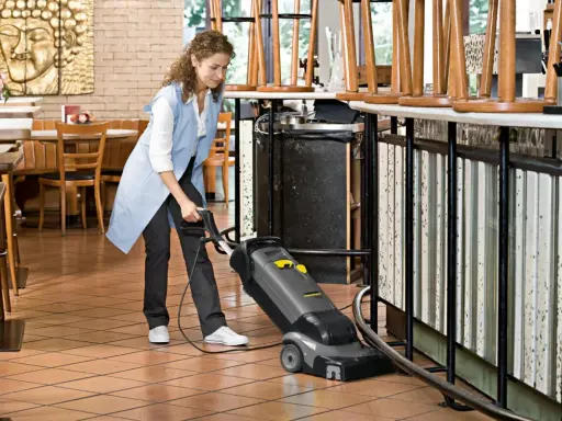 Kobieta sprząta podłogę w restauracji za pomocą odkurzacza. Dowiedz się, czym czyścić linoleum domowe sposoby.